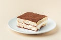 Homemade tiramisu cake on white plate against beige background. Traditional Italian no-bake dessert made of savoiardi, filled with Royalty Free Stock Photo