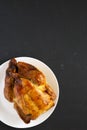 Homemade traditional rotisserie chicken on a white plate on a black background, top view. Flat lay, overhead, from above. Copy