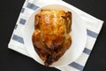 Homemade traditional rotisserie chicken on a white plate on a black surface, top view. Flat lay, overhead, from above