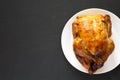 Homemade traditional rotisserie chicken on a white plate on a black surface, top view. Flat lay, overhead, from above. Copy space