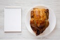 Homemade traditional rotisserie chicken on a white plate, blank notepad, top view. Flat lay, overhead, from above