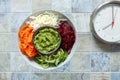 Homemade vegetarian Poke bowl fresh raw carrots, cabbage, cucumber, beets and pesto with alarm clock, Intermittent fasting concept