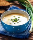 Homemade vichyssoise cream soup served with chives, in blue bowl on wooden table.