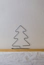 A homemade wire Christmas tree sits on a wooden shelf with white wallpaper symbolizing winter and snow. Royalty Free Stock Photo