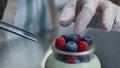 Homemade yogurt with blueberries in a glass jar. Hand putting Strawberry in Yogurt, close up.