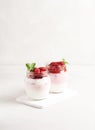 Homemade yogurt with ripe strawberries decorated with mint stands in banks on a wooden stand on a gray background.