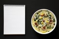 Homemade Zuppa Toscana with Kale and Bread in a white bowl, blank notepad on a black background, top view. Overhead, from above, Royalty Free Stock Photo