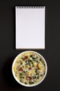 Homemade Zuppa Toscana with Kale and Bread in a white bowl, blank notepad on a black surface, top view. Overhead, from above, flat Royalty Free Stock Photo