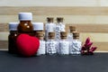 Homeopathic glass bottles of medicine with pink flower buds, red heart on wood and dark background.Homeopathic Medicine for Heart