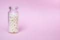 Homeopathic globules in a clear glass bottle on light pink background, alternative homeopathy medicine and naturopathy concept, Royalty Free Stock Photo