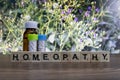 A homeopathy concept - Homeopathic medicine bottles on wooden surface with wild flower background and homeopathy text on table