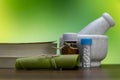 Homeopathy concept Ã¢â¬â A Mortar, rolled leaf with a book and globule bottles on wood surface with yellow green background