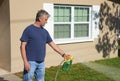 Homeowner man spraying weed killer on the grass in his yard with hose attachment full of chemicals