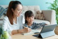 Homeschooling. Asian family with daughter doing homework by using tablet with mother help. Asia mom and child learning online with