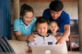 Homeschooling child boy in headphone using laptop computer with happy Asian family togetherness in rural home, parents helping kid Royalty Free Stock Photo