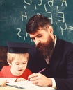 Homeschooling concept. Father checking homework, helps to boy, son. Teacher in formal wear and pupil in mortarboard in Royalty Free Stock Photo