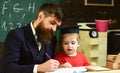 Homeschooling concept. Teacher in formal wear and pupil in mortarboard in classroom, chalkboard on background Royalty Free Stock Photo