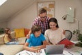 Homeschooling. Young positive parents helping his son with homework while his little sister sitting on sofa on the Royalty Free Stock Photo