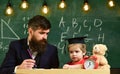 Hometask concept. Enthusiastic kid studying with teacher. Teacher in formal wear and pupil in mortarboard in classroom Royalty Free Stock Photo