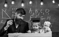 Hometask concept. Teacher in formal wear and pupil in mortarboard in classroom, chalkboard on background. Enthusiastic Royalty Free Stock Photo