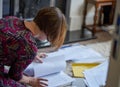 Homework: A young woman, working from home, kneels on rug collating papers.