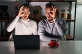 Homosexual couple using computer laptop doing ok gesture shocked with surprised face, eye looking through fingers Royalty Free Stock Photo