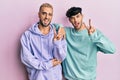 Homosexual gay couple standing together wearing casual clothes smiling with happy face winking at the camera doing victory sign Royalty Free Stock Photo