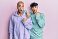 Homosexual gay couple standing together wearing casual clothes surprised pointing with hand finger to the side, open mouth amazed Royalty Free Stock Photo