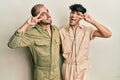 Homosexual gay couple standing together wearing casual jumpsuit doing peace symbol with fingers over face, smiling cheerful Royalty Free Stock Photo