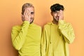 Homosexual gay couple standing together wearing yellow clothes covering one eye with hand, confident smile on face and surprise Royalty Free Stock Photo