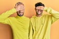 Homosexual gay couple standing together wearing yellow clothes smiling and laughing with hand on face covering eyes for surprise Royalty Free Stock Photo
