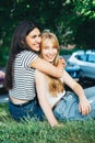 Homosexual women embrace and laugh while sitting on the grass.