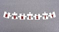 HONESTY - word composed of paper white puzzles on a gray background