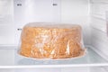 Honey cake packed in cling film in a refrigerator. Frozen cake
