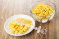 Honey dipper on corn flakes with honey in white saucer, bowl with cornflakes on table