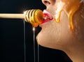 Honey dripping from honey dipper on sexy girl lips. Thick honey dipping from the wooden honey spoon. Beauty model woman Royalty Free Stock Photo