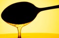 Honey dripping, pouring from dark spoon on yellow background. Thick viscous honey molasses flowing. Close up of golden Royalty Free Stock Photo