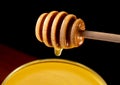 Honey dripping, pouring from honey dipper into glass bowl on black background. Healthy organic thick honey dipping from Royalty Free Stock Photo