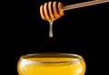 Honey dripping, pouring from honey dipper into glass bowl on black background. Healthy organic thick honey dipping from Royalty Free Stock Photo