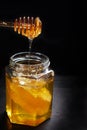 Honey dripping from spoon into glass jar with comb