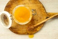 Honey dripping from a wooden dipper and glass jar on old cutting board on white wooden rustic background