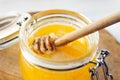 Honey dripping from a wooden dipper in jar on old cutting board on white wooden rustic background