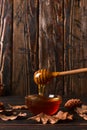 Honey flows from a stick into a jar. Rustic sweet autumn photo, wooden background and dry leaves, copy space