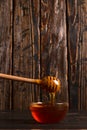 Honey flows from a stick into a jar. Rustic sweet photo, wooden background, copy space