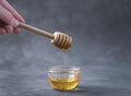 Honey flows from a wooden stick into a glass bowl on a dark background close-up. The concept of healthy and organic food