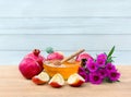 Honey in glass bowl, wooden honey dipper, red apples, garnet and pink flowers on wooden table on a blue planks background Royalty Free Stock Photo