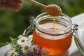 Honey in glass jar with bee flying and flowers on a wooden floor Royalty Free Stock Photo