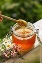 Honey in glass jar with bee flying and flowers on a wooden floor Royalty Free Stock Photo