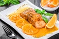 Honey Glazed fillet salmon with orange slices, spices and basil on white plate on dark background. Delicious dish of seafood