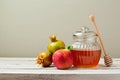 Honey jar, red apples and pomegranate on white wooden board